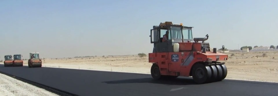A picture of construction machines and compactors smoothening the layer of asphalt 
